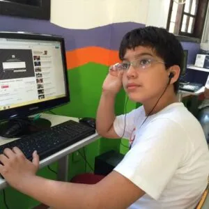 Menino jovem usando fones de ouvido enquanto está sentado em frente a um computador