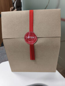 Caixa de presente do kit de boas-vindas da Bradesco Seguros, com um laço vermelho e o adesivo da campanha '(abrace) o presente'.