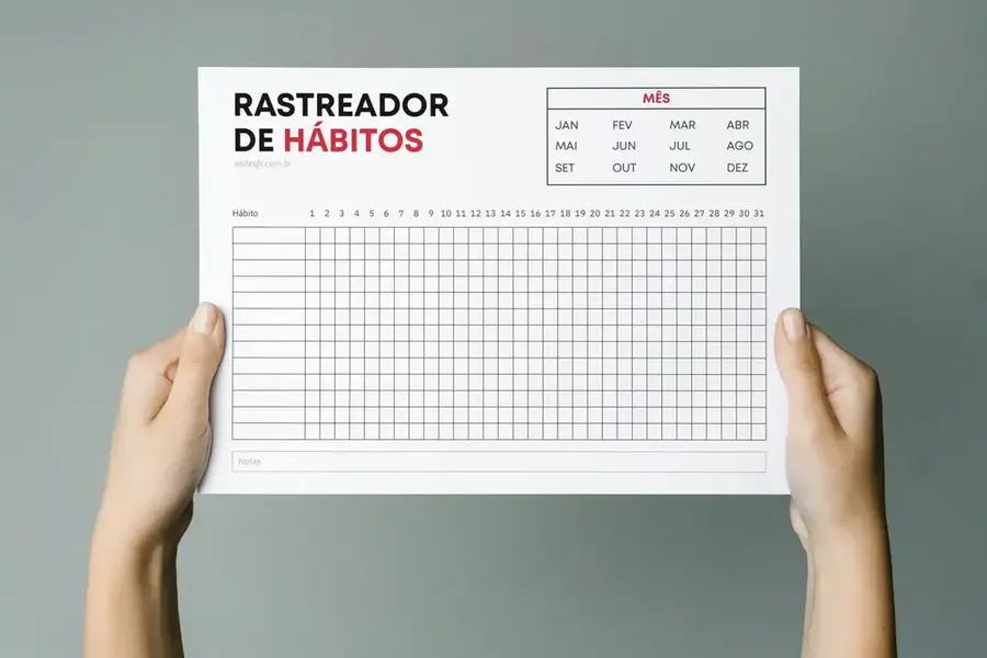 Duas mãos segurando a folha do Rastreador de Hábitos em PDF para impressão, mostrando seu layout limpo com grade para acompanhamento diário de rotinas.