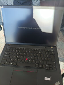 Notebook corporativo, um Lenovo ThinkPad, aberto sobre o colo com a mensagem 'Estamos preparando tudo para você' na tela durante a configuração inicial.