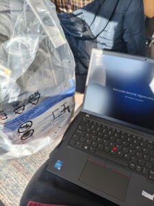 Tela do novo notebook da empresa exibindo a mensagem 'Isso pode demorar alguns minutos', um momento de espera no primeiro dia de trabalho juntamente a uma mochila dentro de um saco plástico.