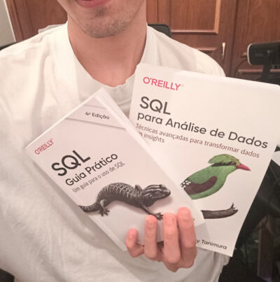 Close-up do autor segurando dois livros da O'Reilly sobre SQL. O livro à esquerda é "SQL Guia Prático" e o à direita é "SQL para Análise de Dados", focando em técnicas avançadas.