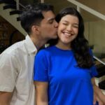 O autor do blog dando um beijo no rosto de sua namorada, Laura, durante a celebração de Ano Novo de 2024 para 2025. Ele veste uma camisa branca e ela sorri alegremente usando um conjunto azul vibrante.